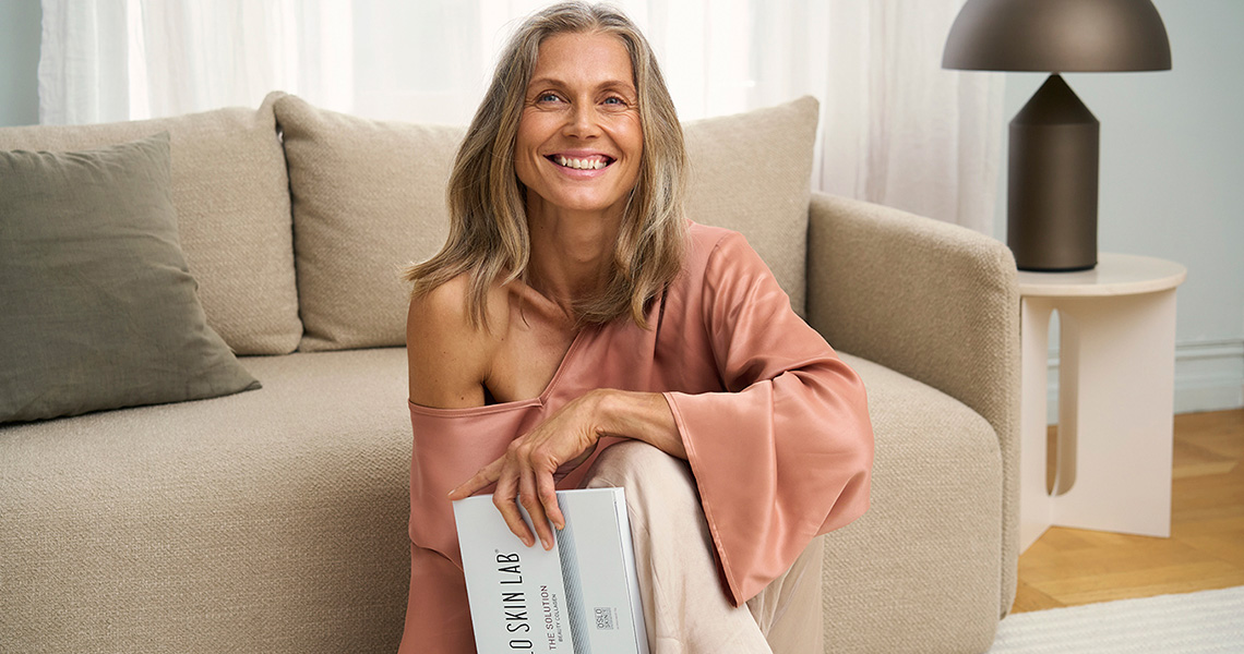 Woman sitting in front of couch holding a The Solution collagen package.jpg